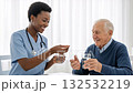A young female nurse gives medication to an elderly man. Friendly caregiver helping a senior patient take a pill with water. Elder care and assisted living concept A young female nurse gives medication to an elderly man. Friendly caregiver helping a senior patient take a pill with water. Elder care and assisted living concept 132532219