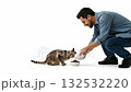 A man crouches down to feed his tabby cat on a white background. A caring pet owner pours dry food into a bowl for his hungry kitten. The concept of pet care and companionship A man crouches down to feed his tabby cat on a white background. A caring pet owner pours dry food into a bowl for his hungry kitten. The concept of pet care and companionship 132532220