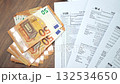 US tax forms spread out methodically displaying detailed financial information and calculation, stack of 50-euro banknotes placed on wooden table slow motion 132534650