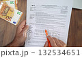 Male accountant analyzes details on W-4 tax form with pen, man works at table with euro bills and laptop ensuring document complies with tax regulations slow motion 132534651