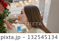 Close-up of lady smelling decorative plant in shopping mall with festive lights in background, blurred view of people enhances vibrant holiday atmosphere with warm lighting 132545134