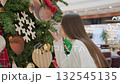 Side view of lady smelling decorative plant in shopping mall, with festive decorations and lights in background, blurred people in background 132545135