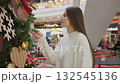 Side view of lady smelling decorative plant in shopping mall, with decorative lights in background, other people are visible in background 132545136