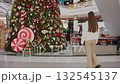 Back view of lady walking towards restaurant with large decorative flower in front, other shoppers are visible in background, with festive mall decorations and vibrant shopping atmosphere 132545137