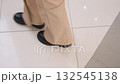 Leg view of individual wearing black boots walking on modern tiled floor towards a beautiful tree, reflections on the floor and stylish, contemporary indoor environment with seasonal decor 132545138