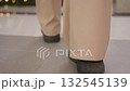 Rear leg view of person wearing black boots walking on well-tied floor towards decorative plant, urban structure in background with light reflections on ground 132545139