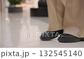 Leg view of person wearing black boots walking on well-tied floor toward decorative plant, urban structure in background, showcasing modern indoor environment with clean floor and stylish design 132545140