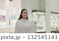 Girl in white walking in modern shopping mall towards decorative Christmas plant, bright lights and retail displays create a vibrant atmosphere, showcasing holiday spirit and festive decor 132545143