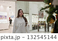 White girl walking towards decorative plant in bright shopping mall, with hair flowing down her back, blurred background shows another person walking, showcasing stylish and vibrant atmosphere 132545144