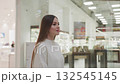Young woman walking towards decorative plant in modern shopping mall, with long flowing hair, bright and stylish atmosphere with retail displays and glass cabinets in background 132545145