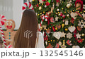 Back view of white woman walking towards festive Christmas tree with holiday decorations inside modern shopping mall, candy canes, stars, ornaments, and lights creating joyful atmosphere 132545146