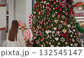 Back view of woman walking towards festive holiday tree with, Christmas decorations inside modern shopping mall, beautiful ornaments, candy canes, and gingerbread man near Christmas tree 132545147