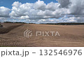 A large red tractor planting seeds in a vast, freshly tilled field under a dramatic cloudy sky, signifying farm work 132546976
