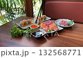 Woman Hand With Chopsticks Dipping Sushi Roll into Soy Sauce. Close Up. Girl eating sushi with salmon on outdoor terrace of Japanese restaurant 132568771