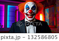 A clown dressed in a tuxedo and vibrant makeup brings joy to guests in a stylish venue. 132586805