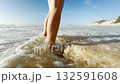 Close up of a woman legs standing barefoot on the shore of the Atlantic Ocean. Waves splash around feet. Summer vacation, relaxation, travel, freedom, and beach lifestyle 132591608