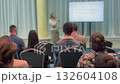 Presenter gives lecture to audience during conference with screen display in bright room 132604108