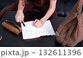 The left-handed woman in a red T-shirt closes the notebook, puts away her pen, closes her pencil case, and puts everything into a large brown bag. 132611396
