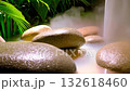 large smooth stones with rising mist, tropical palm leaves framing scene, cascading water column in background, wet textured surfaces and golden highlights creating grounding spa mood 132618460