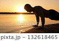 man exercises by water, individual strengthening muscles during early morning by lakeside shore, athlete actively performing deep pushup routines beside tranquil water body at sunrise 132618465