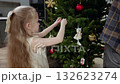 Young girl decorating festive christmas tree, hanging delicate ornaments with care while father watching nearby, creating warm holiday moment 132623274