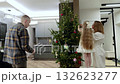Family decorating christmas tree together, parents helping young girl hanging ornaments in minimalist living space, creating holiday warmth 132623277