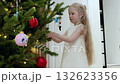Young girl decorating christmas tree, hanging colorful ornaments with care and festive spirit, creating holiday magic at home 132623356