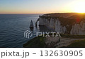 Iconic chalk cliffs and turquoise waters of Etretat glow under sunlight, showcasing Normandy's natural beauty and peaceful coastline. 132630905