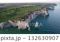 Iconic chalk cliffs and turquoise waters of Etretat glow under sunlight, showcasing Normandy's natural beauty and peaceful coastline. 132630907
