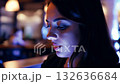 A young woman focuses intently on her mobile device while seated in a cozy cafe illuminated by soft, ambient lighting. The atmosphere is relaxed and modern, perfect for unwinding 132636684