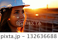At a construction site during sunset, a woman wearing a helmet takes a moment to appreciate the beautiful evening light. Her serene expression indicates her connection to the environment 132636688