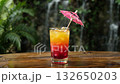 Colorful Tropical Drink With a Tiny Umbrella on a Wooden Table by a Waterfall 132650203