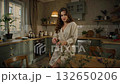Woman in Cozy Kitchen Enjoying Morning Light While Relaxing in Robe and Surrounded by Plants and Breakfast 132650206