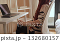 A woman with long, flowing hair is seated at a sleek, modern desk, animatedly gesturing as she interacts with her laptop. She embodies the essence of a dynamic and vibrant workfromhome atmosphere 132680157