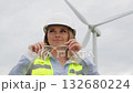 A highly skilled female engineer, dressed in safety gear, stands confidently in a wind farm, showcasing her expertise and knowledge in the rapidly evolving field of renewable energy technology 132680224