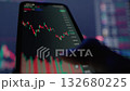 This image shows a closeup of a modern smartphone displaying realtime stock market data, featuring candlestick charts and colorful indicators in a vibrant digital trading environment 132680225