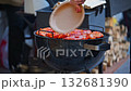 A person is cooking meat on a grill. The meat is red and he is well-cooked 132681390