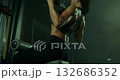 focused female athlete executes a vertical block pull to her chest in a dark gym. The atmosphere is intense showcasing her strength and dedication during her workout. 132686352