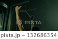 dedicated female athlete performs a vertical block pull focusing on strength training in a gym. The setting features dim lighting enhancing the intense atmosphere of the evening workout. 132686354