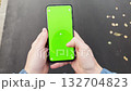 Close-up handheld view of person walking and using smartphone with green screen 132704823