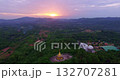 A stunning aerial view of a golden pagoda nestled amidst lush green hills during a vibrant sunset, with dramatic clouds and soft sunlight casting a serene glow over the landscape. 132707281