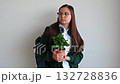 Smiling teenage student holding her plant, standing against a clean white background, ready for school or study. 132728836