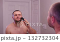 Man trimming beard with electric trimmer in bathroom mirror. 132732304