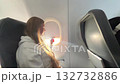 Woman lifting window shade and looking outside during airplane flight. 132732886