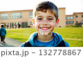 Close up view of a Caucasian pupil boy with backpack standing next the school. Cheerful pupil boy smiles brightly while standing next to his school with backpack. 132778867