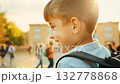 Close up view of a Caucasian pupil boy with backpack standing next the school. Cheerful pupil boy stands proudly near school, backpack secure and smile wide. 132778868