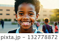 Close up view of an African American pupil boy with backpack standing next the school. Bright-eyed pupil boy stands near school, smiling warmly at the camera lens. 132778872