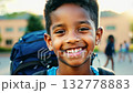 Close up view of an African American pupil boy with backpack standing next the school. Close-up of schoolboy smiling warmly near school with backpack on his back. 132778883