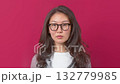 Confident young woman with glasses against bright red background, looking serious.  132779985