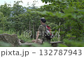 A man sitting on a bench in the middle of a dense green forest stares into the distance, relaxing in nature 132787943